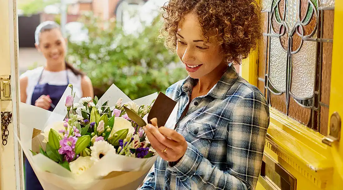 woman in checked shirt receiving a delivery of flowers at her door with the delivery woman in the background showcasing biosecurity on imported flowers