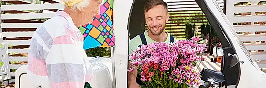 image of a delivery man in a van handing a beautiful bunch of purple carnations to an elderly lady for flower delivery Brisbane