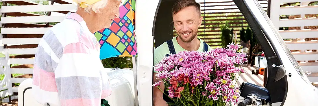 image of a delivery man in a van handing a beautiful bunch of purple carnations to an elderly lady for flower delivery Brisbane
