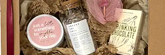 close up of flower delivery with gifts with soy candle, calming bath soak and drinking chocolate