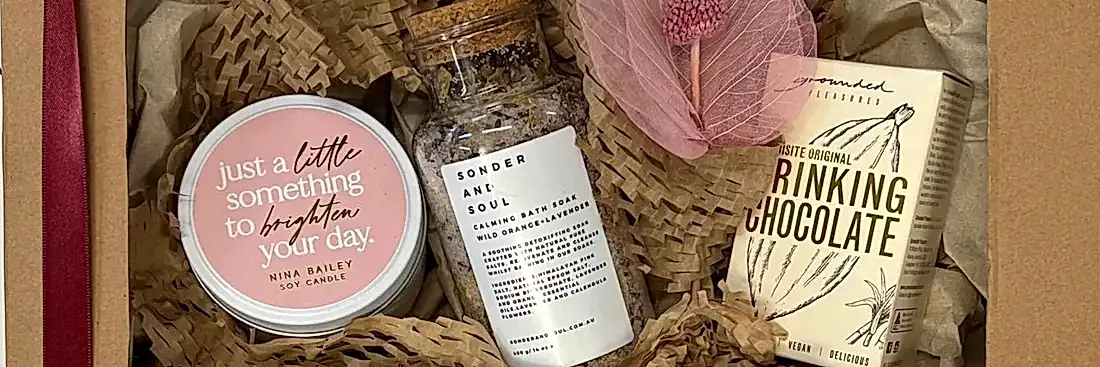 close up of flower delivery with gifts with soy candle, calming bath soak and drinking chocolate